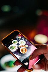 hand with smartphone photographing food at restaurant or cafe