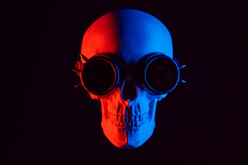 human skull in steampunk glasses with red and blue neon light on a black background