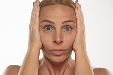 Middle aged blond woman tightens her face with her hands on a white background