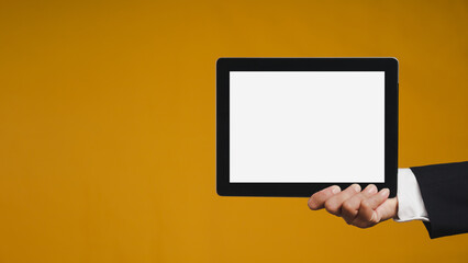 Hand holding a blank black screen tablet against an orange background.