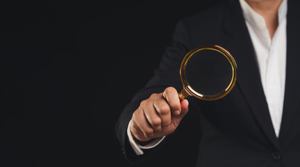 Close-up of a businessman's hand holding a magnifying glass while standing on a black background