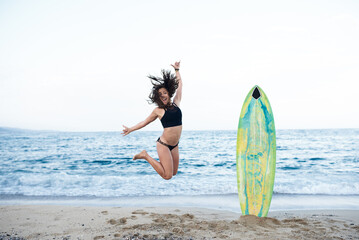 Naklejka na ściany i meble Female surfer jumping on beach
