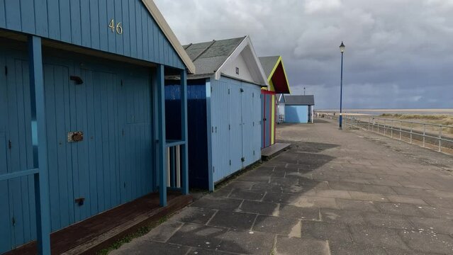 Colorful beach huts stood in a line along the seafront with sandy beach and moody grey sky’s. UK