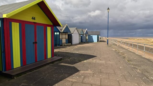 Colorful beach huts stood in a line along the seafront with sandy beach and moody grey sky’s. UK