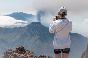Tourist girl takes picture of Cumbre Vieja volcanic eruption on the island of La Palma, Canary Islands. Volcano La Palma from far aerial view.	