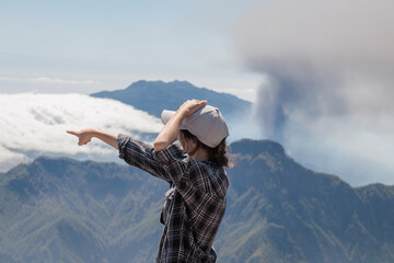 Tourist girl pointing next to Cumbre Vieja volcanic eruption on the island of La Palma, Canary Islands. Volcano La Palma from far aerial view..