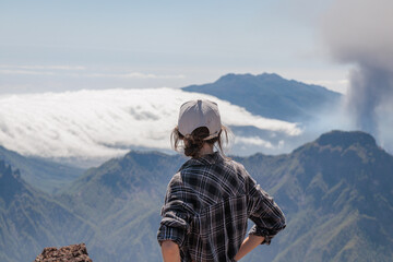 Tourist girl watching Cumbre Vieja volcanic eruption on the island of La Palma, Canary Islands. Volcano La Palma from far aerial view..