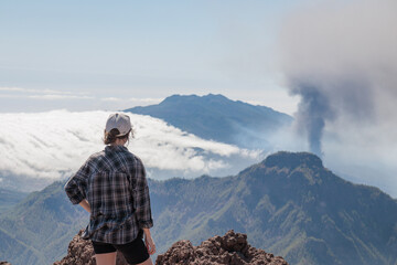 Tourist girl watching Cumbre Vieja volcanic eruption on the island of La Palma, Canary Islands. Volcano La Palma from far aerial view..