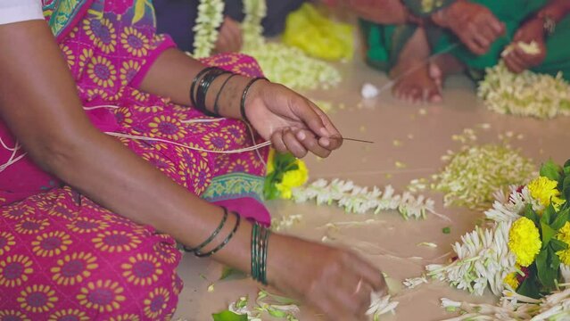 A video shows female hands skillfully crafting flower garlands inside a house