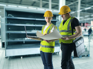 Engineers in supermarket. Retail equipment installers. Large refrigerator for store. Man and woman engineers. Installation of refrigeration equipment. Refrigeration chambers for supermarket