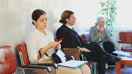 Unemployed young woman is waiting for job interview in waiting room. Bored female applicant with smartphone is waiting for invitation to recruiter s office