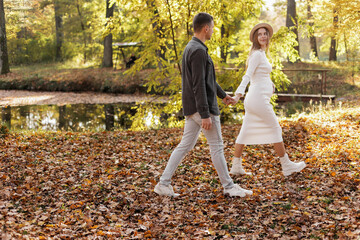 couple, man and pregnant wife are holding hands and walking in the autumn park on sunset. Happy family enjoying pregnancy on nature. The concept of Mother's Day and Women's Day.