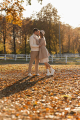 Young stylish couple lovers are hugging and kissing in the autumn park. Lovely romantic moment between man and woman in love, looking to each others. Happy family. Love, youth, happiness concept.