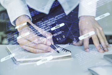 Multi exposure of abstract software development hologram with world map and hand writing in notebook on background with laptop, global research and analytics concept