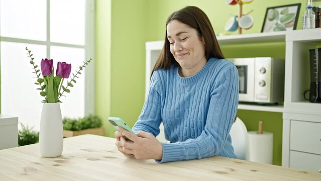 Young caucasian woman using smartphone sitting on table at dinning room