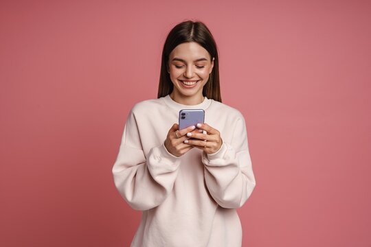 Positive Woman Smiling While Using Smartphone Isolated Over Pink Background