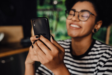 Smiling african woman using smartphone while sitting in kitchen