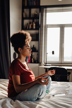 Afro woman meditating while sitting in lotus pose on bed