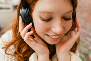 Cheerful girl listening music with headphones while sitting outdoors