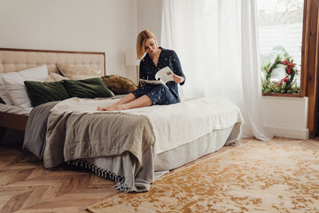 Beautiful woman reading magazine while sitting in bed in her apartment