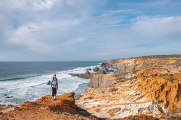 Joyful expression of a young backpacker standing on the edge of a cliff overlooking the Atlantic Ocean in the Odemira region, western Portugal. Wandering along the Fisherman Trail, Rota Vicentina