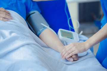 Female doctor using blood pressure monitor and stethoscope to check blood pressure on male patient in hospital.