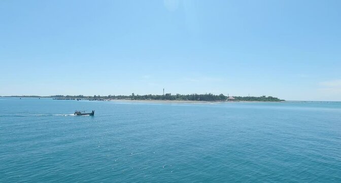 A small island in the middle of the blue sea and crossing a fishing boat into it.