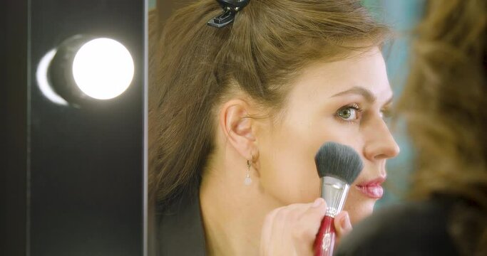 Close-up view of a young woman applying makeup in front of mirror before dating.