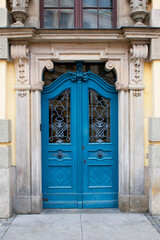 View of an old blue door with decorative elements on the facade of an antique building with beige and yellow walls, columns and sculptures. Poland, Wroclaw, January 2023.
