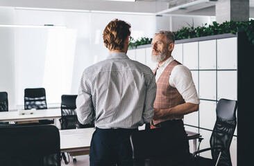 Senior boss speaking to young employee in modern office