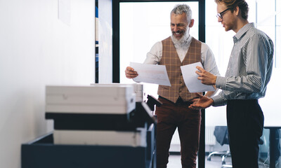 Cheerful colleagues discussing papers in office printer room