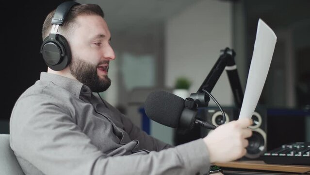 A handsome radio host in headphones speaks into a microphone during a radio broadcast.