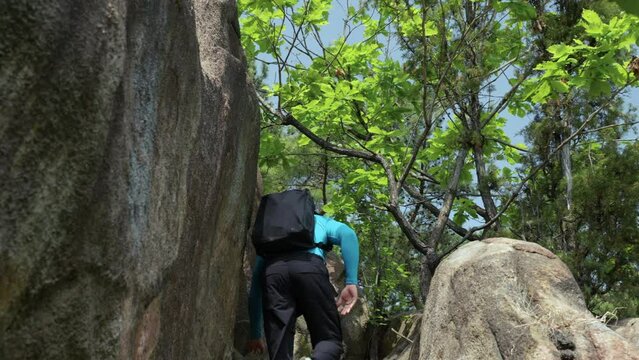 Confident male free solo climber rock climbing in Gwanaksan Mountain Forest - low angle rear following view behind