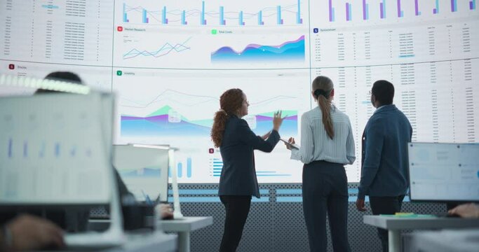 Low Angle Shot: Financial Data Analysts Studying Information And Graphs On Big Digital Screen In Modern Monitoring Office. Multiethnic Employees Working Infront Of Desktop Computers In Consulting Firm