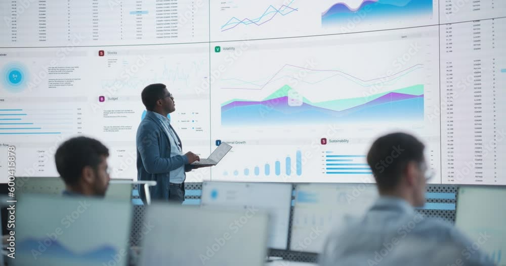 Aufkleber Male Project Manager Using Laptop And Analyzing Information, Graphs On Big Digital Screen In Monitoring Office. Black Man Working For Deep Learning Company, Diverse Employees Behind Desktop Computers.