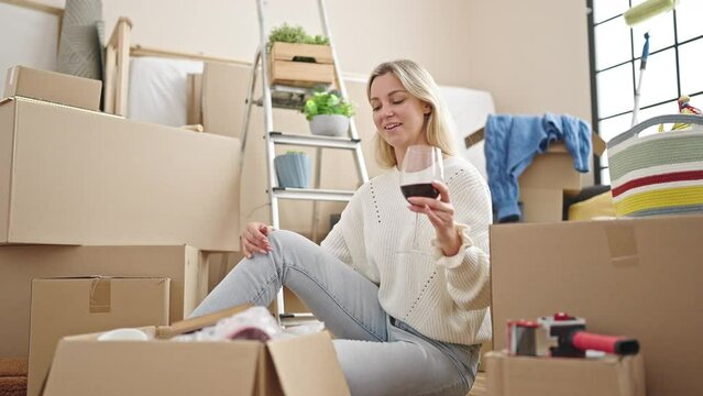 Young blonde woman holding glass of wine looking photography at new home