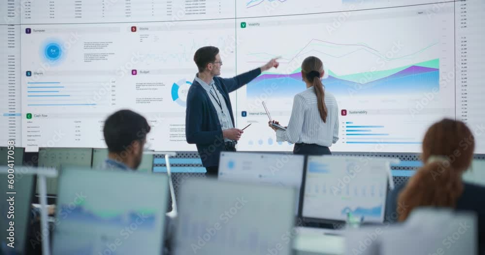 Poster Male Data Scientist And Female Project Manager Discussing Reports And Graphs On Big Digital Screen In Modern Monitoring Office. Diverse Employees Working Behind Computers in Deep Learning Company.