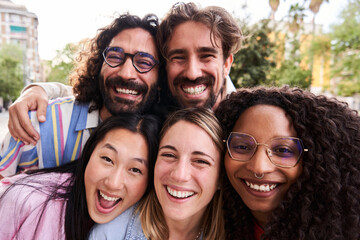 Close up portrait of a group of multicultural friends looking at camera cheerfully with heads together. Young people having fun outdoors enjoying the sunny day.