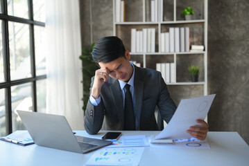 Frustrated young businessman working on a laptop computer sitting at his working place in office.