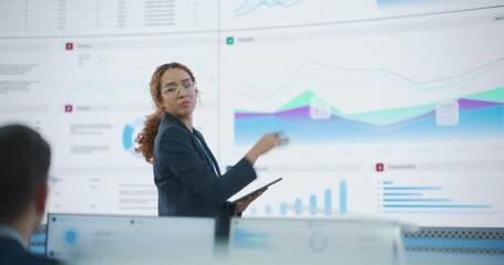 Hispanic Female Senior Data Scientist Reviewing Reports Of Risk Management Department On Big Digital Screen In Monitoring Room. Diverse Consulting Company Employees Working Behind Desktop Computers. - Powered by Adobe