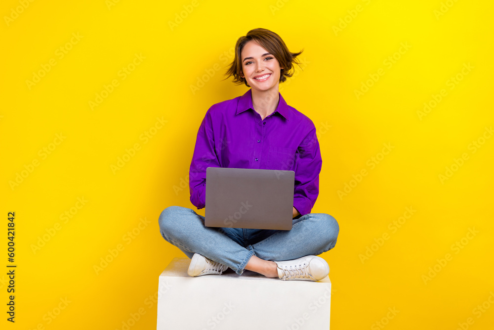 Poster full body photo of cheerful nice lady sit cube podium use wireless netbook isolated on yellow color 