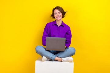Full body photo of cheerful nice lady sit cube podium use wireless netbook isolated on yellow color...