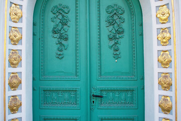 Part of old green round door with decorative elements and golden moldings on a white wall around....