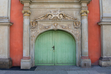 Fototapeta na wymiar View of the old round green door with golden decorative ancient elements around and columns on the orange color facade of the old building. Historical architecture. Poland, Gdansk, April 2023