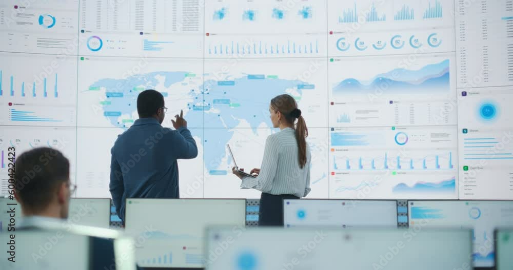 Poster back view of black male analyst talking to caucasian female manager in front of big digital screen w