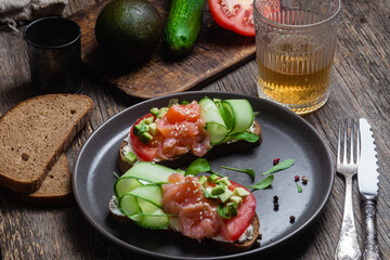 Black bread sandwich with salted salmon, cream cheese, tomato and cucumber in a plate