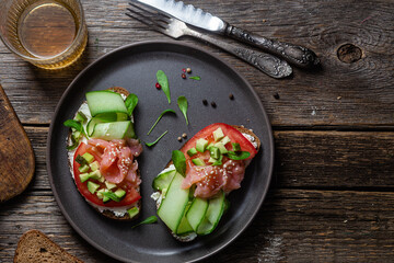Black bread sandwich with salted salmon, cream cheese, tomato and cucumber in a plate