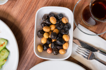 Olives in a white bowl on a wooden table, top view. breakfast.