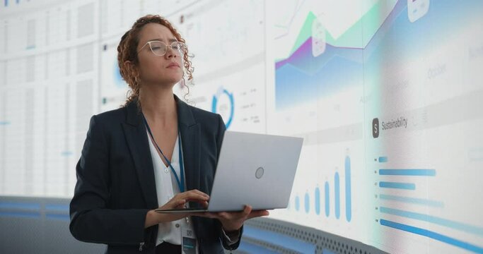 Successful Hispanic Businesswoman Holding Laptop Computer And Reviewing Financial Reports On Digital Screen In Monitoring Office. Female Leader Running Deep Learning, Artificial Intelligence Company.