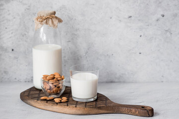 Organic almond milk in a glass bottle next to an almond on a stylish wooden board on a stone table. Natural eco-friendly products.